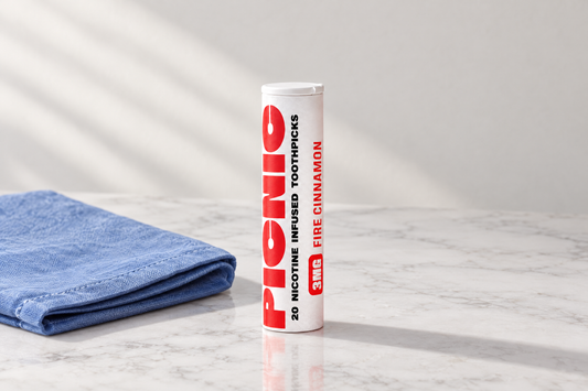 A Picnic Fire Cinnamon nicotine toothpick tube on white marble beside a folded blue linen napkin