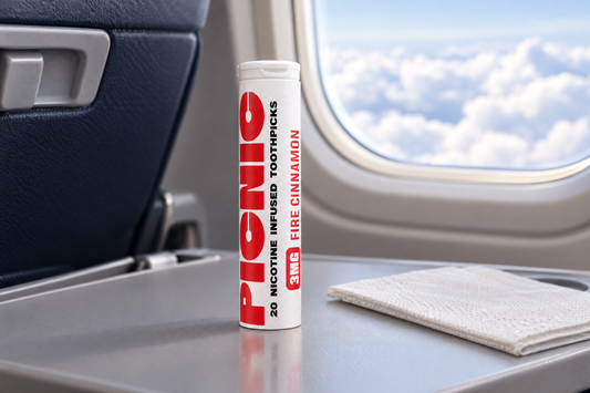 A Picnic Fire Cinnamon nicotine toothpick tube standing on an airplane tray table by the window